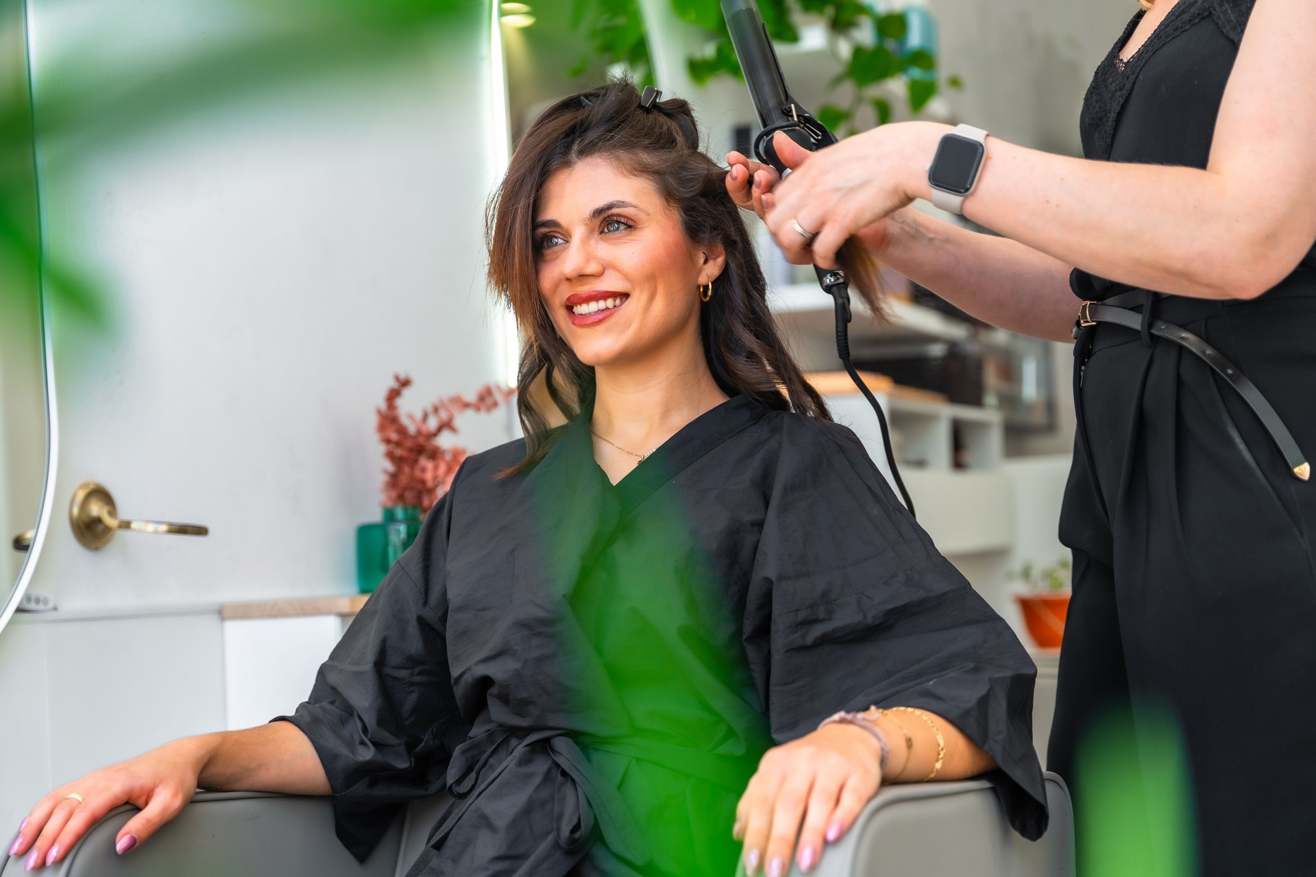 Hairdresser using curling iron on client's hair in beauty salon