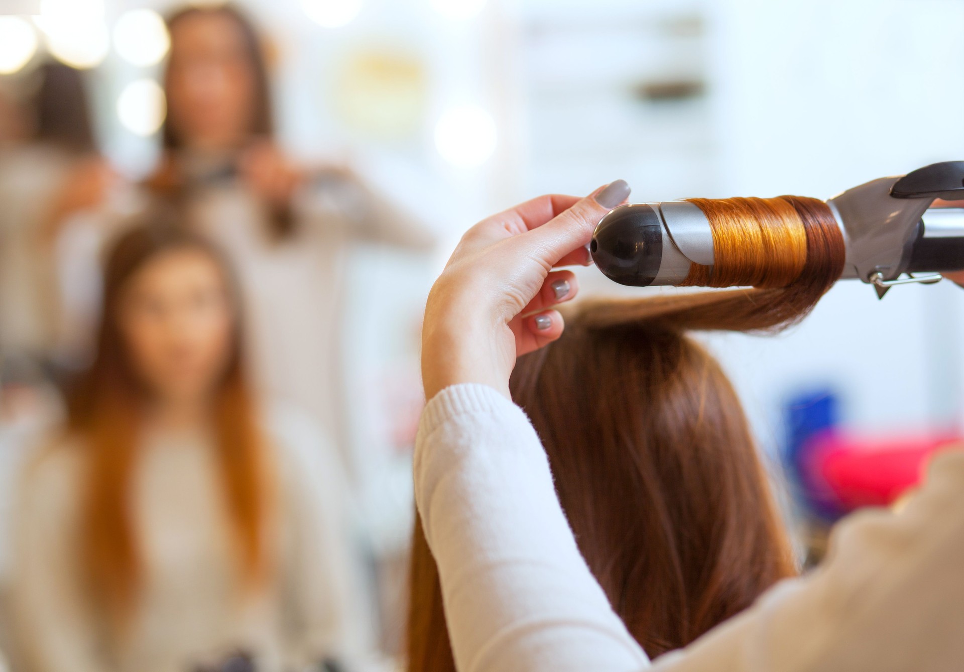 Hairdresser makes hairstyle girl with long red hair in a beauty salon. Create curls with curling irons.