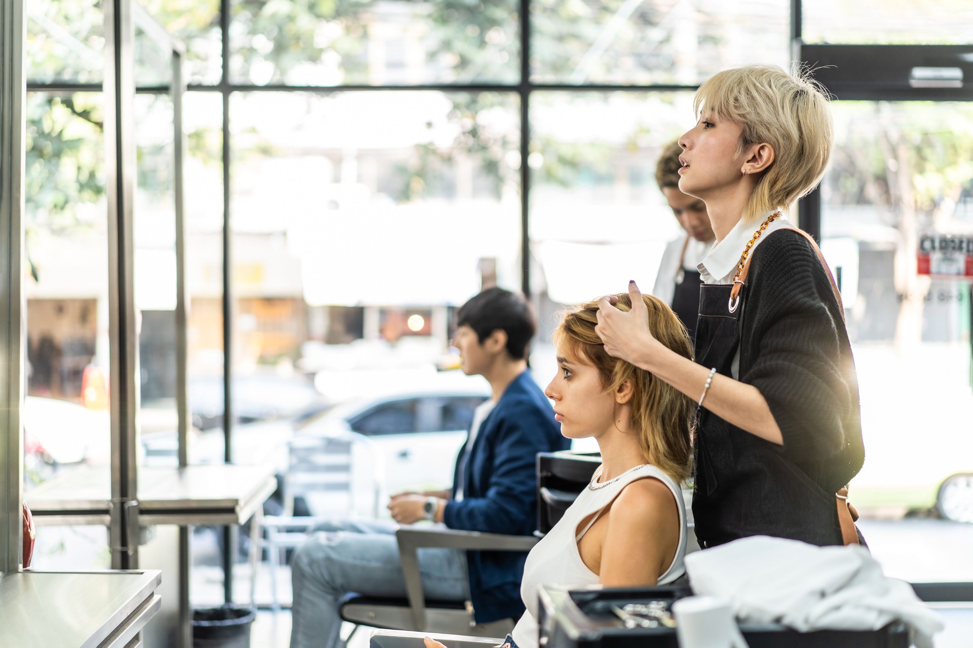 Asian professional female stylist cutting woman's hair in salon. The woman hairdresser using scissors cut the young girl sitting in the shop looking at mirror with smile. Beauty salon business concept